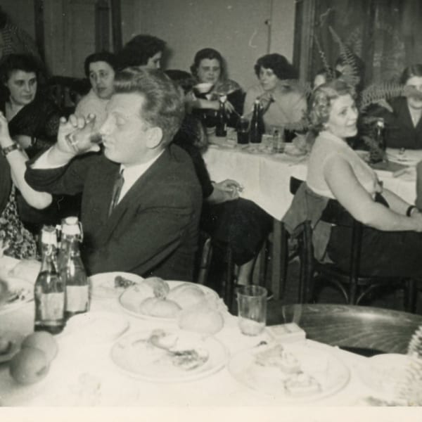 Black and white photo of people dining at Helfeld's Delicatessen, a man drinking from a glass.