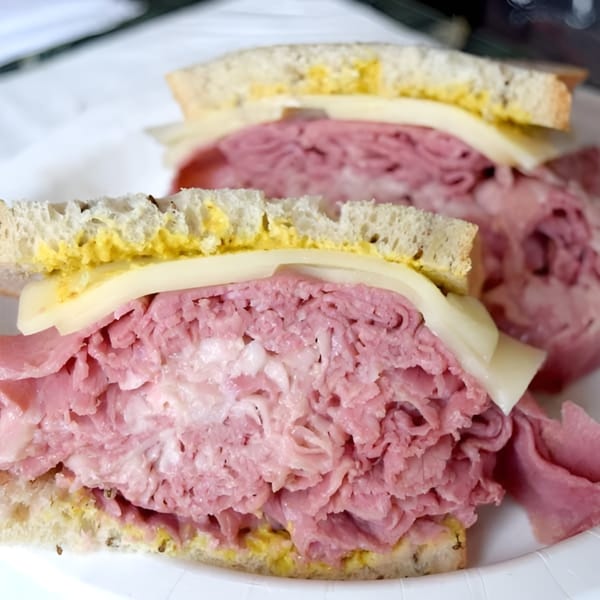 Two Helfeld's Delicatessen sandwiches with thick-cut pastrami, cheese, and mustard on rye bread.