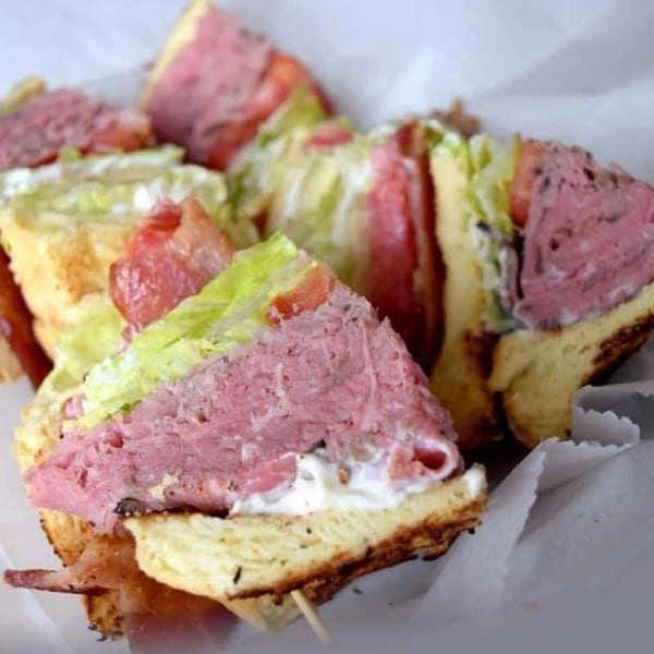 Close-up of Helfeld's Delicatessen sandwiches with corned beef, lettuce, tomato, and bacon on toasted bread.