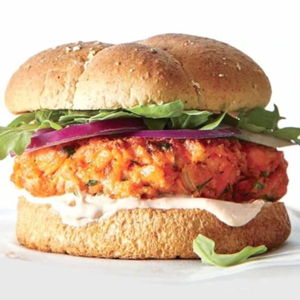 Helfeld's Delicatessen & Catering salmon burger with red onion, arugula, and sauce on a bun.