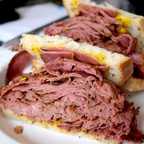 A Helfeld's Delicatessen pastrami sandwich, overflowing with meat and mustard on white bread.