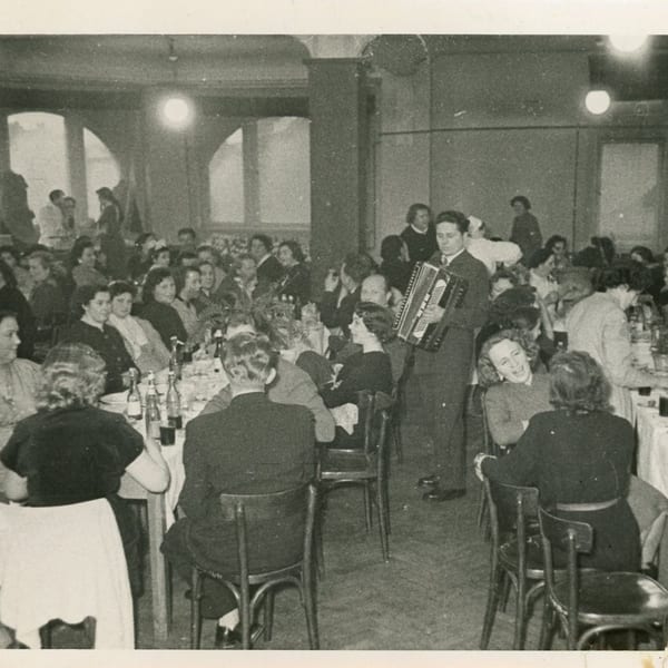 A musician playing an accordion for guests seated at tables in a lively Helfeld's Delicatessen.